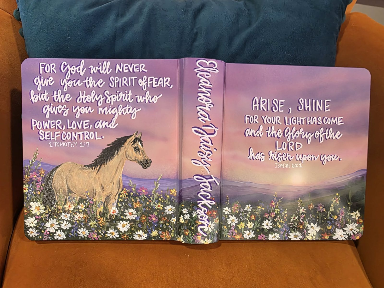 Hand-painted Bible cover for Eleanora Daisy Jackson with a buckskin horse in a wildflower meadow under a lavender sunset, lettered with 2 Timothy 1:7 and Isaiah 60:1