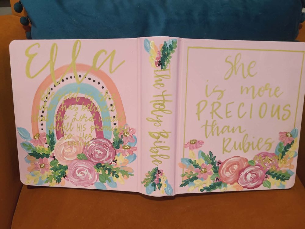 Pink hand-painted Bible cover for Ella with rainbow, Proverbs verse, and floral accents