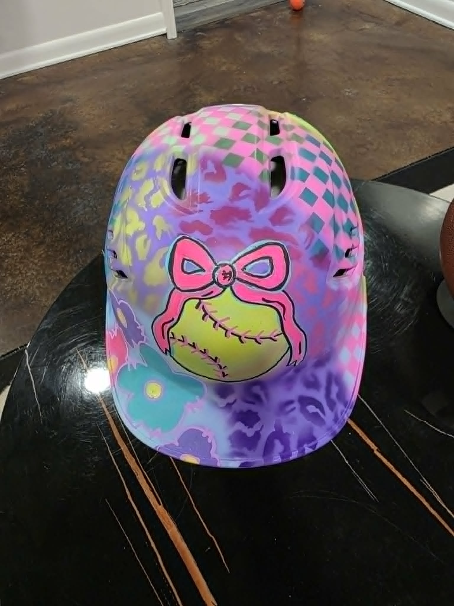 Custom airbrushed pastel softball helmet with leopard print, checkerboard, and pink bow on a yellow softball