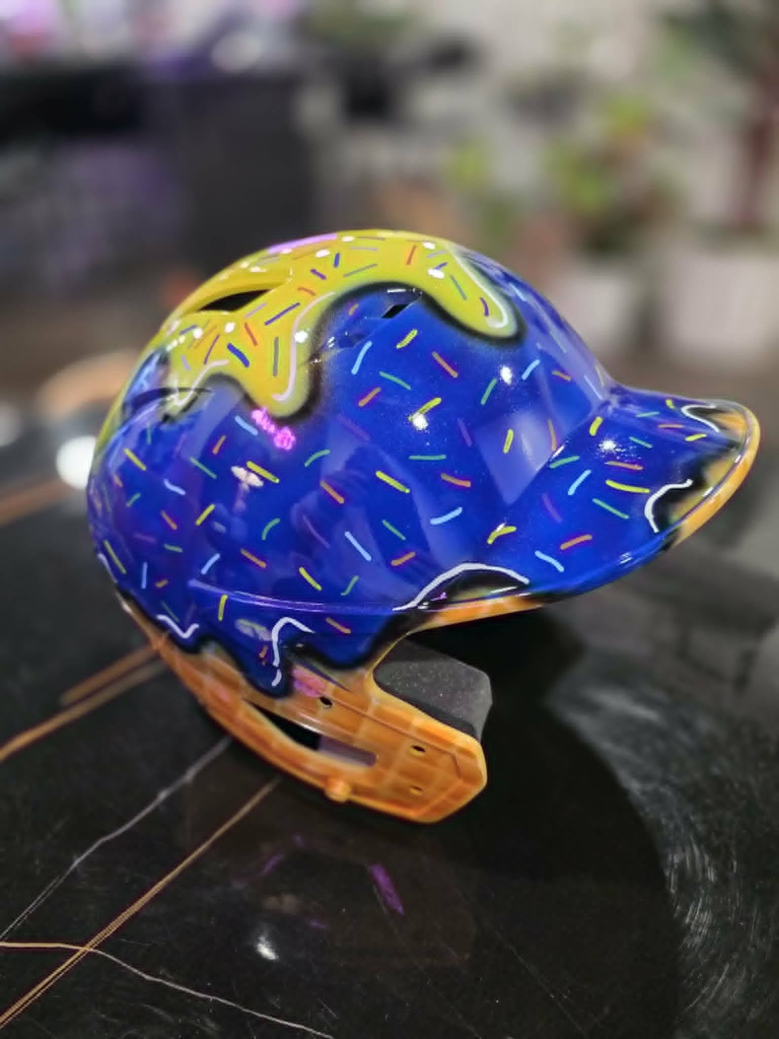 Custom airbrushed blue softball helmet painted as a sprinkled donut with yellow icing drips