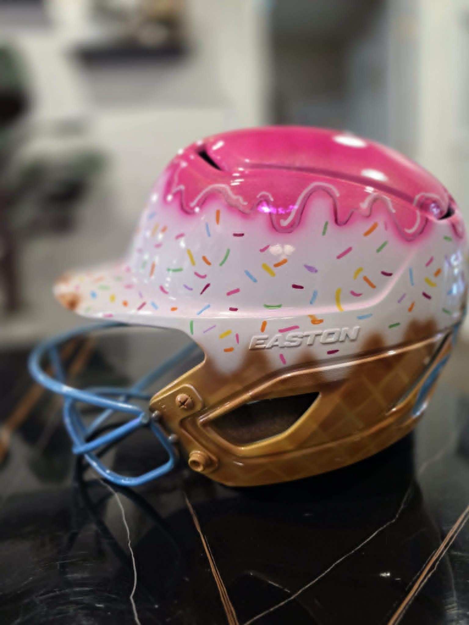 Custom airbrushed Easton softball helmet painted as a pink ice cream cone with rainbow sprinkles and a waffle cone bottom