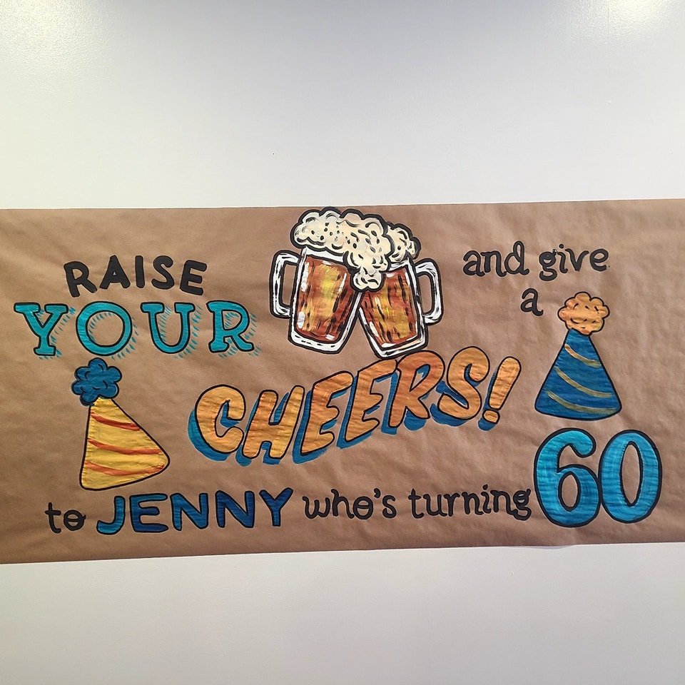 Hand-painted 60th birthday banner reading 'Raise Your Cheers to Jenny who's turning 60' with painted beer mugs and party hats