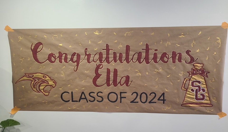 Hand-painted graduation banner reading 'Congratulations Ella, Class of 2024' in maroon script with Spring Garden Panthers logo and cheerleader megaphone