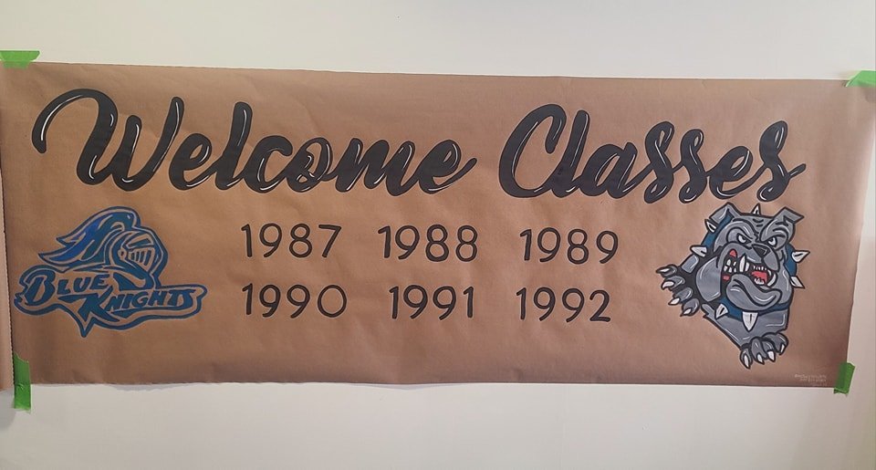 Hand-painted class reunion banner reading 'Welcome Classes 1987-1992' in black script with Blue Knights and Bulldogs school mascots