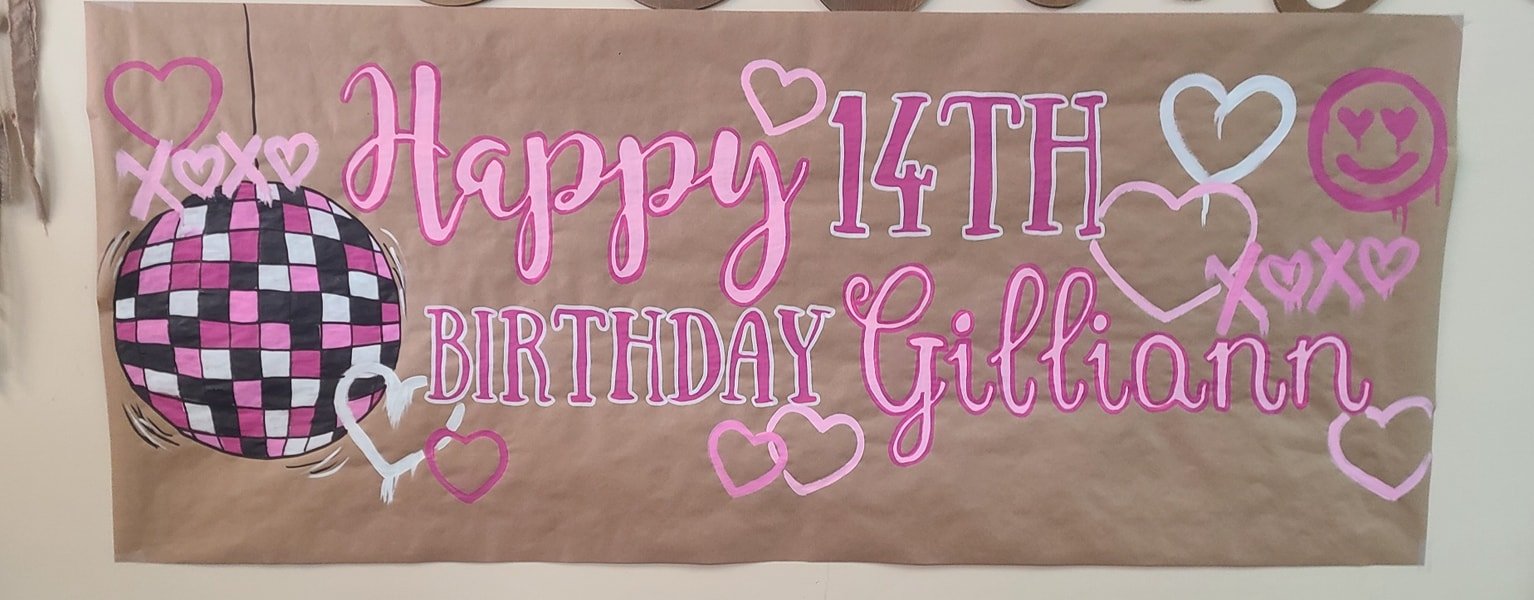 Hand-painted 14th birthday banner reading 'Happy 14th Birthday Gilliann' in pink script with disco ball, hearts, and graffiti smiley face