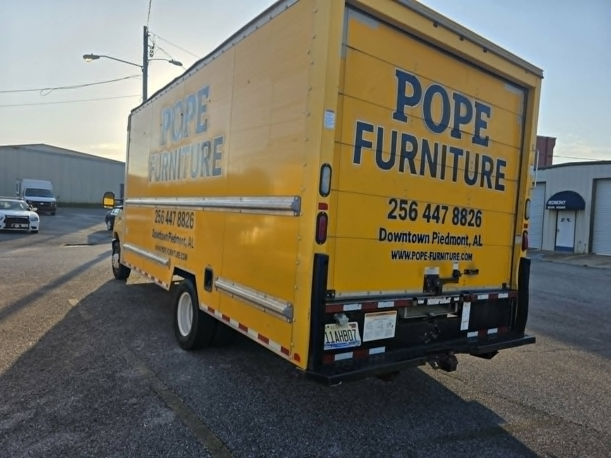 Rear three-quarter view of the yellow Pope Furniture box truck with hand-painted black lettering on both sides