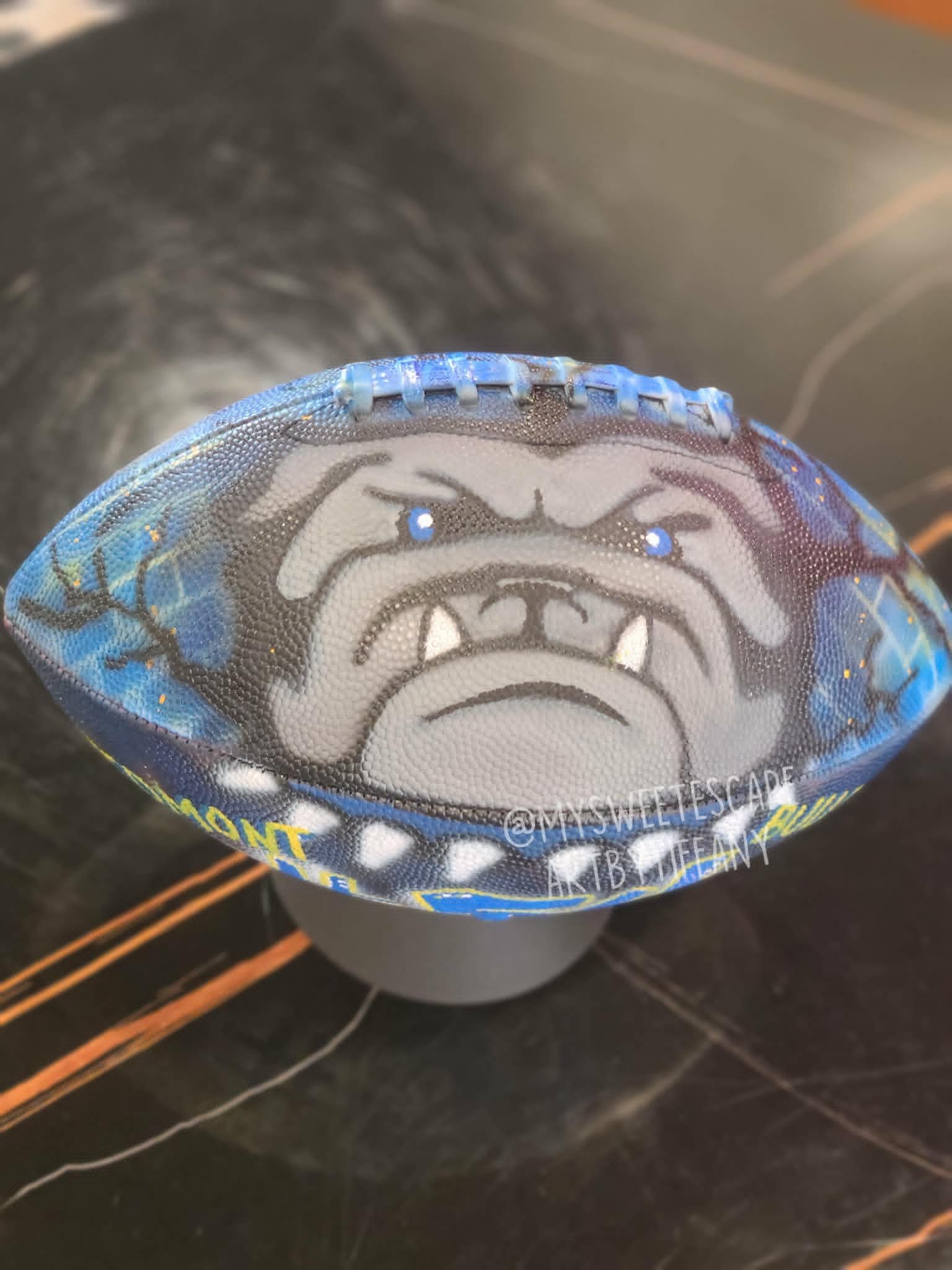 Hand-painted blue football with fierce Piedmont Bulldogs mascot and chain-link fence detail in school colors