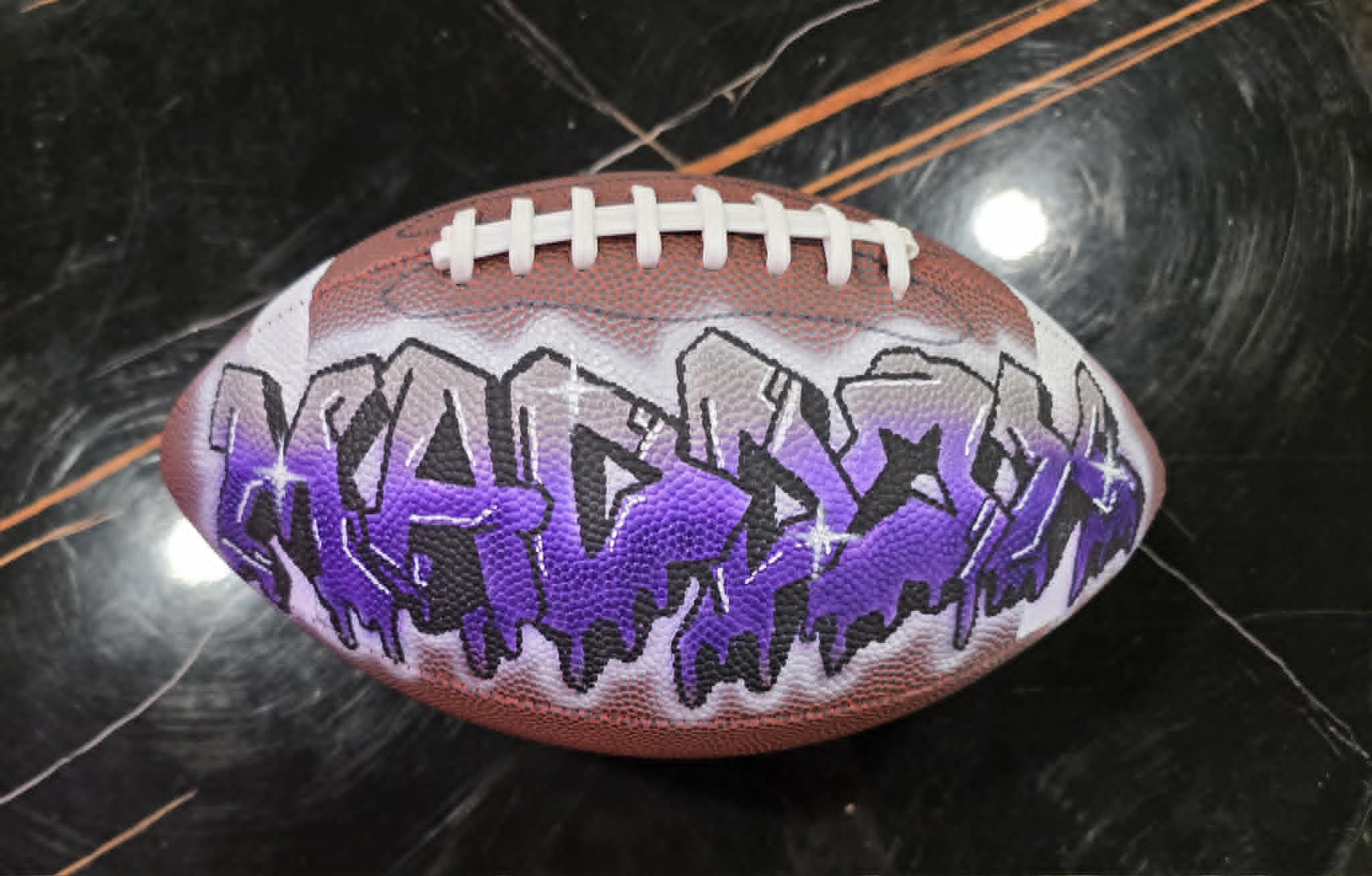Hand-painted football with 'Mason' in dripping purple, silver, and black graffiti lettering with star accents