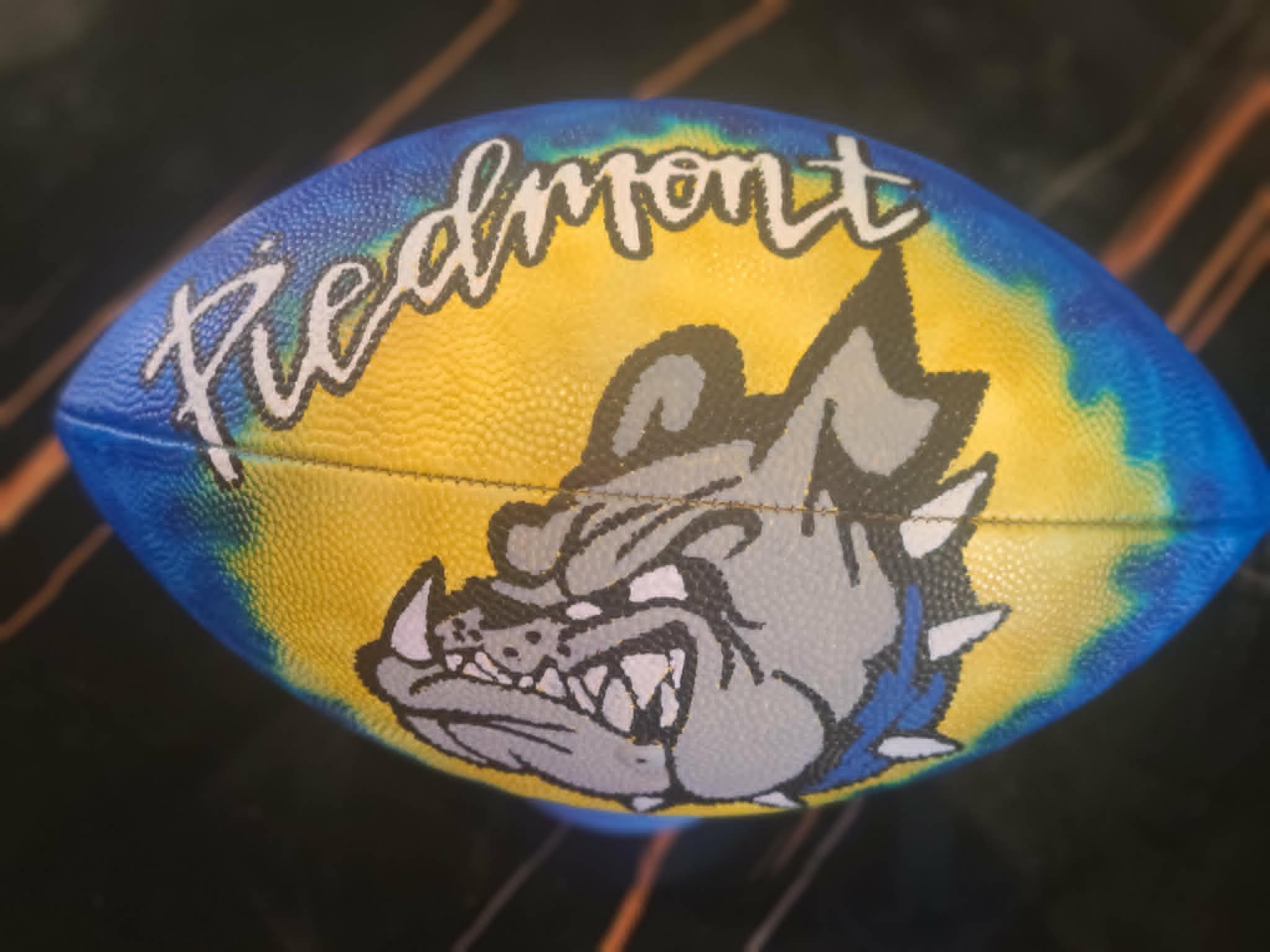 Hand-painted Piedmont Bulldogs football with bold script 'Piedmont' lettering, blue and yellow fade, and gray bulldog mascot