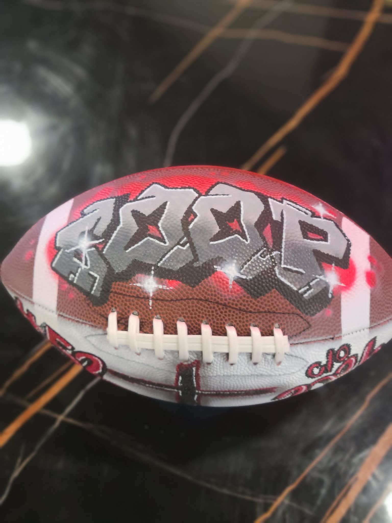 Hand-painted football with silver and red graffiti lettering, star accents, and white striping