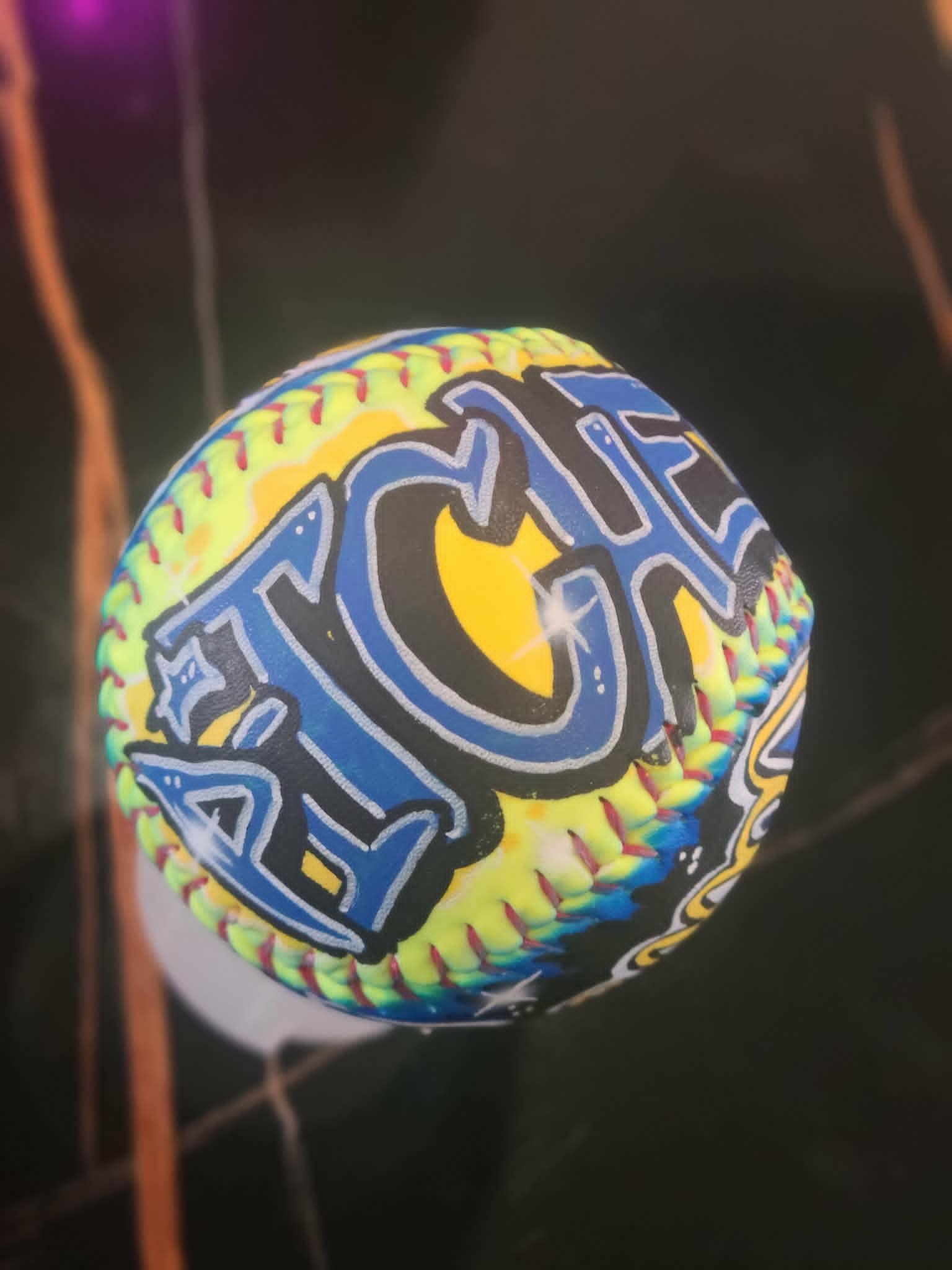 Airbrushed yellow softball with bold blue and white graffiti-style team lettering