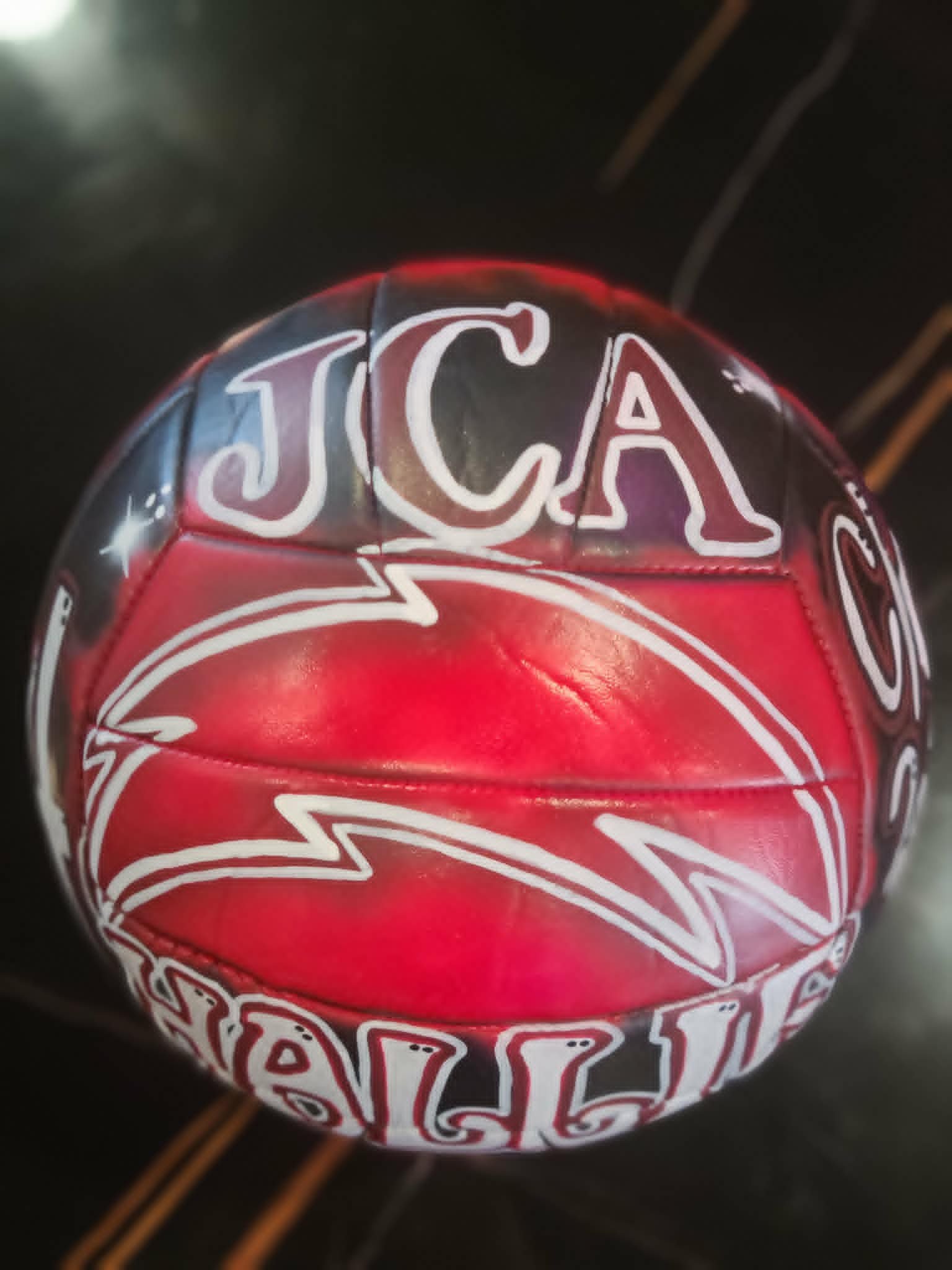 Hand-painted JCA volleyball in maroon, black, and white with bold serif lettering and lightning bolt accents