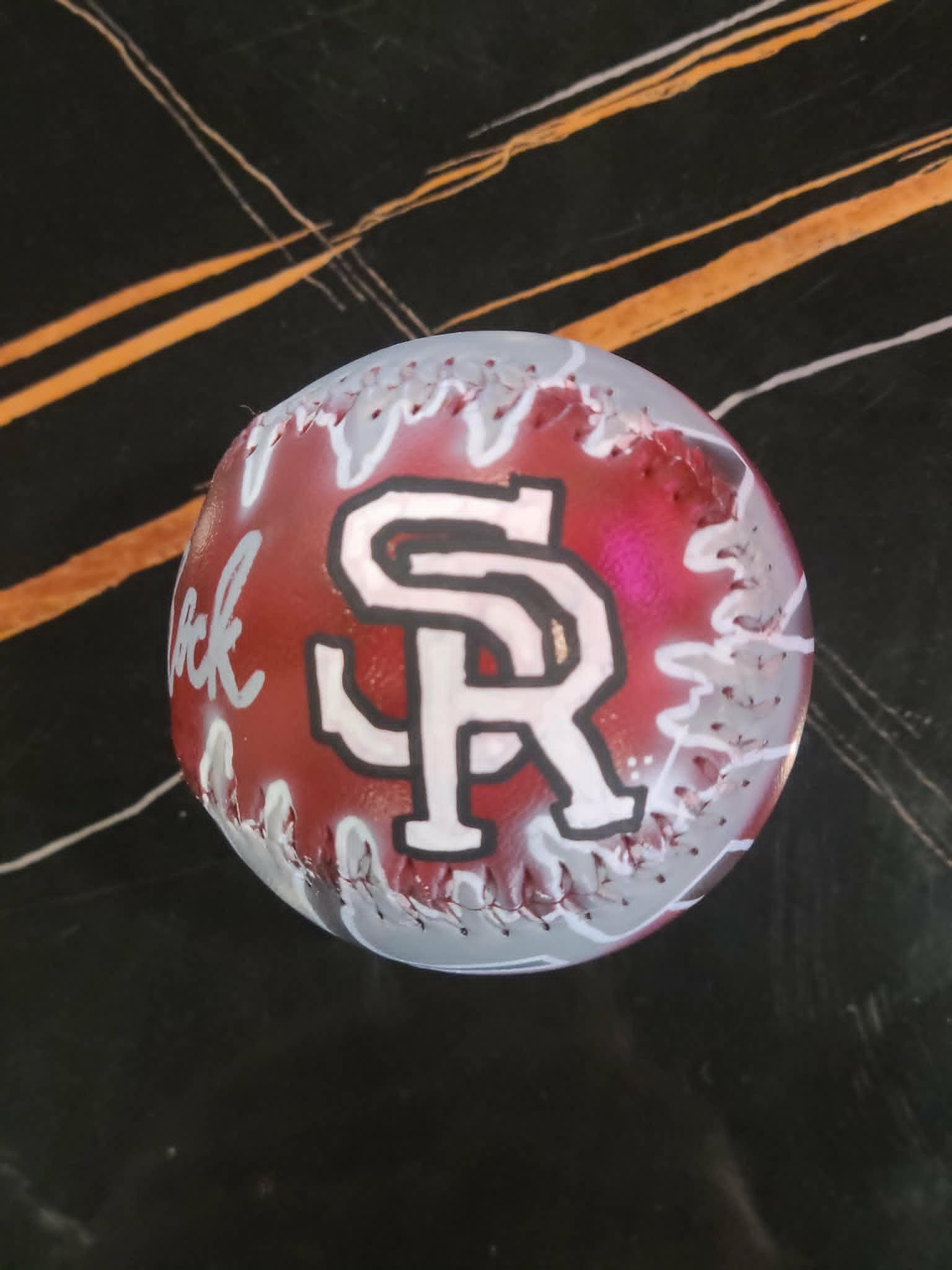 Airbrushed maroon and gray baseball with bold white interlocking 'SR' Sand Rock varsity logo