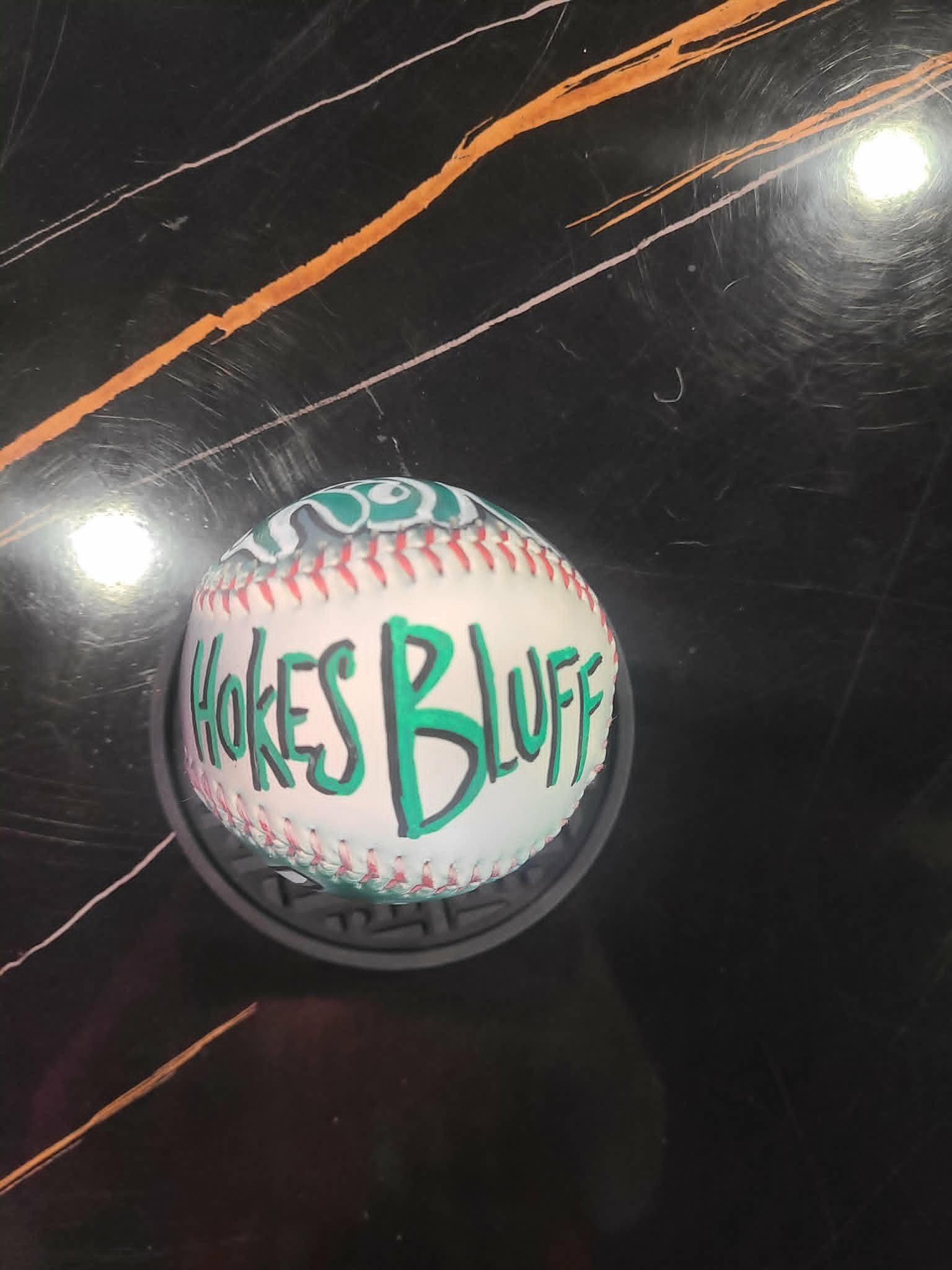Hand-painted Hokes Bluff baseball with bold green graffiti-style lettering on a white ball
