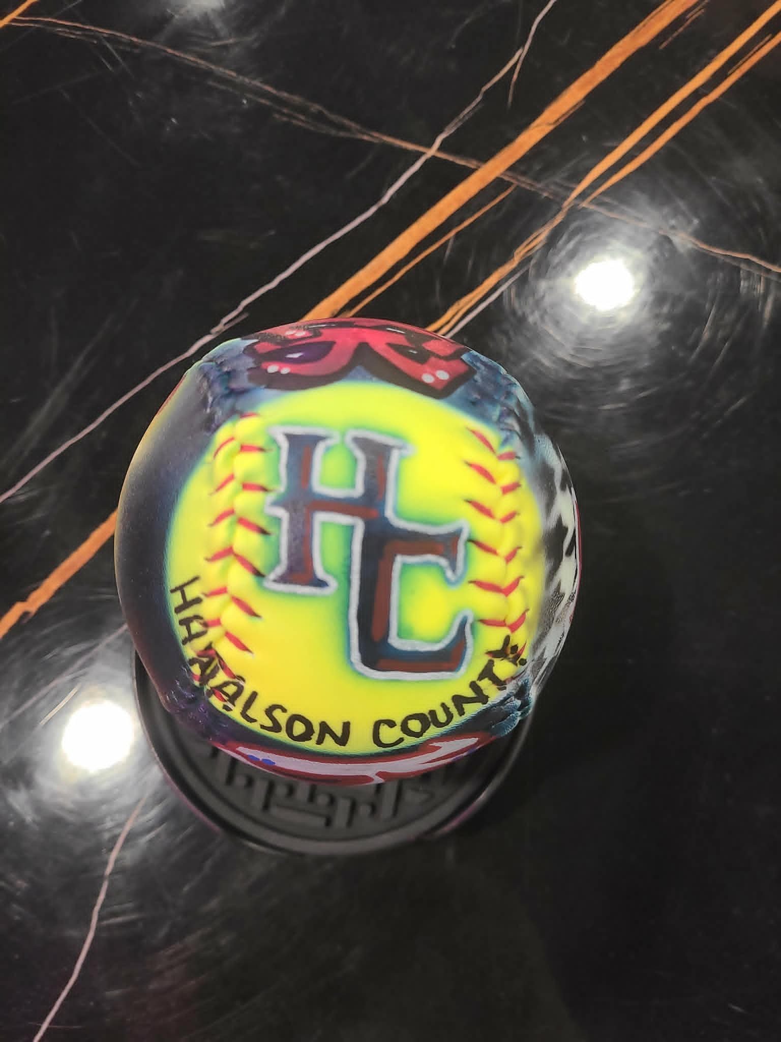 Airbrushed Haralson County softball with bold 'HC' team initials and yellow, red, and black color burst