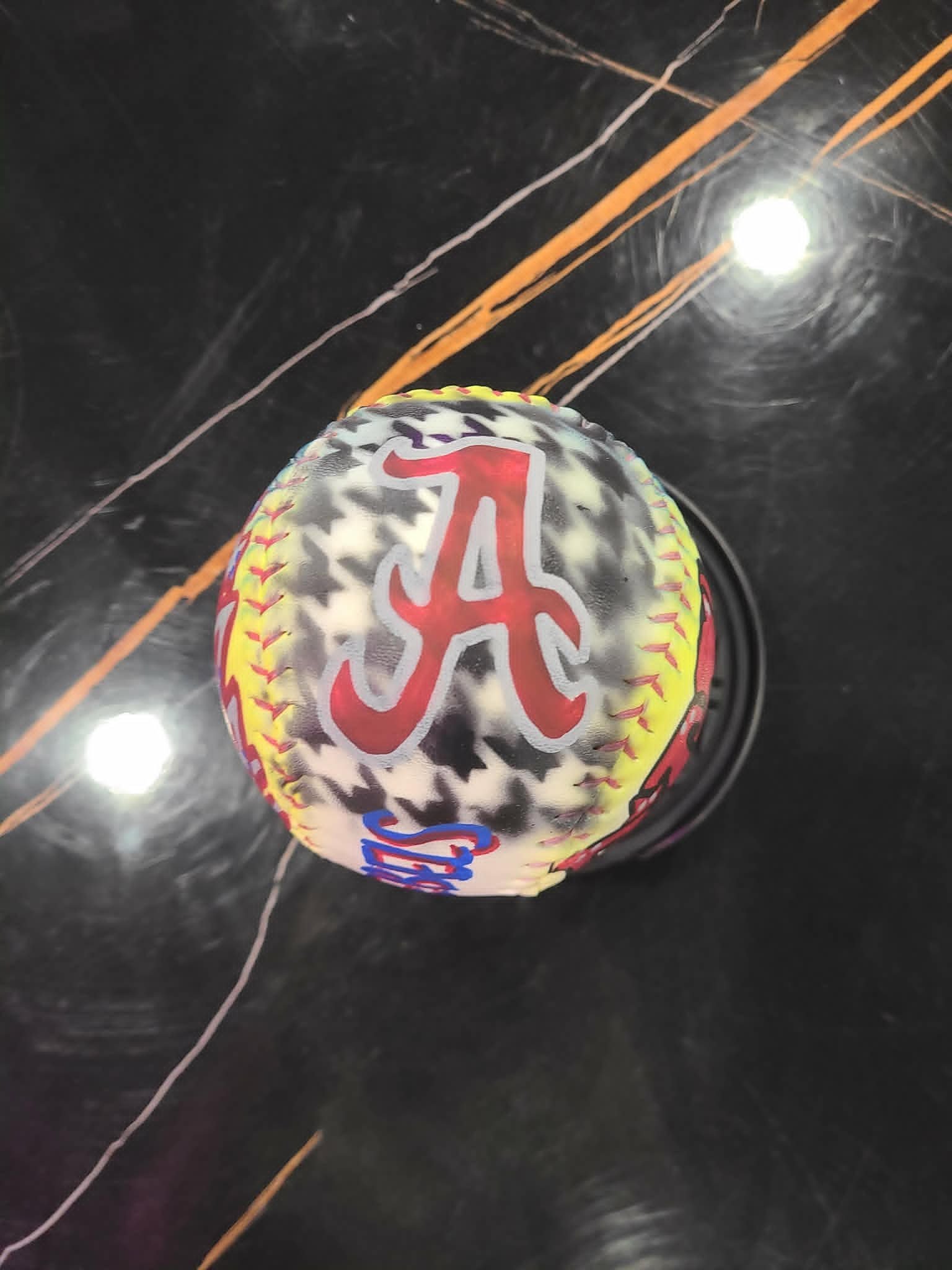 Airbrushed Alabama Crimson Tide softball with iconic red script 'A' logo on a tie-dye yellow, black, and white background