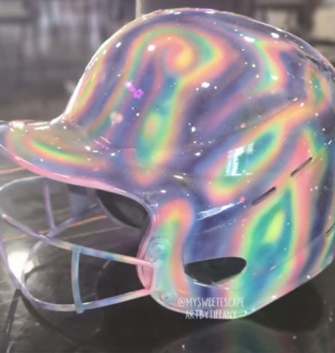 Custom airbrushed holographic rainbow oil-slick batting helmet with swirling iridescent colors and a starry galaxy effect