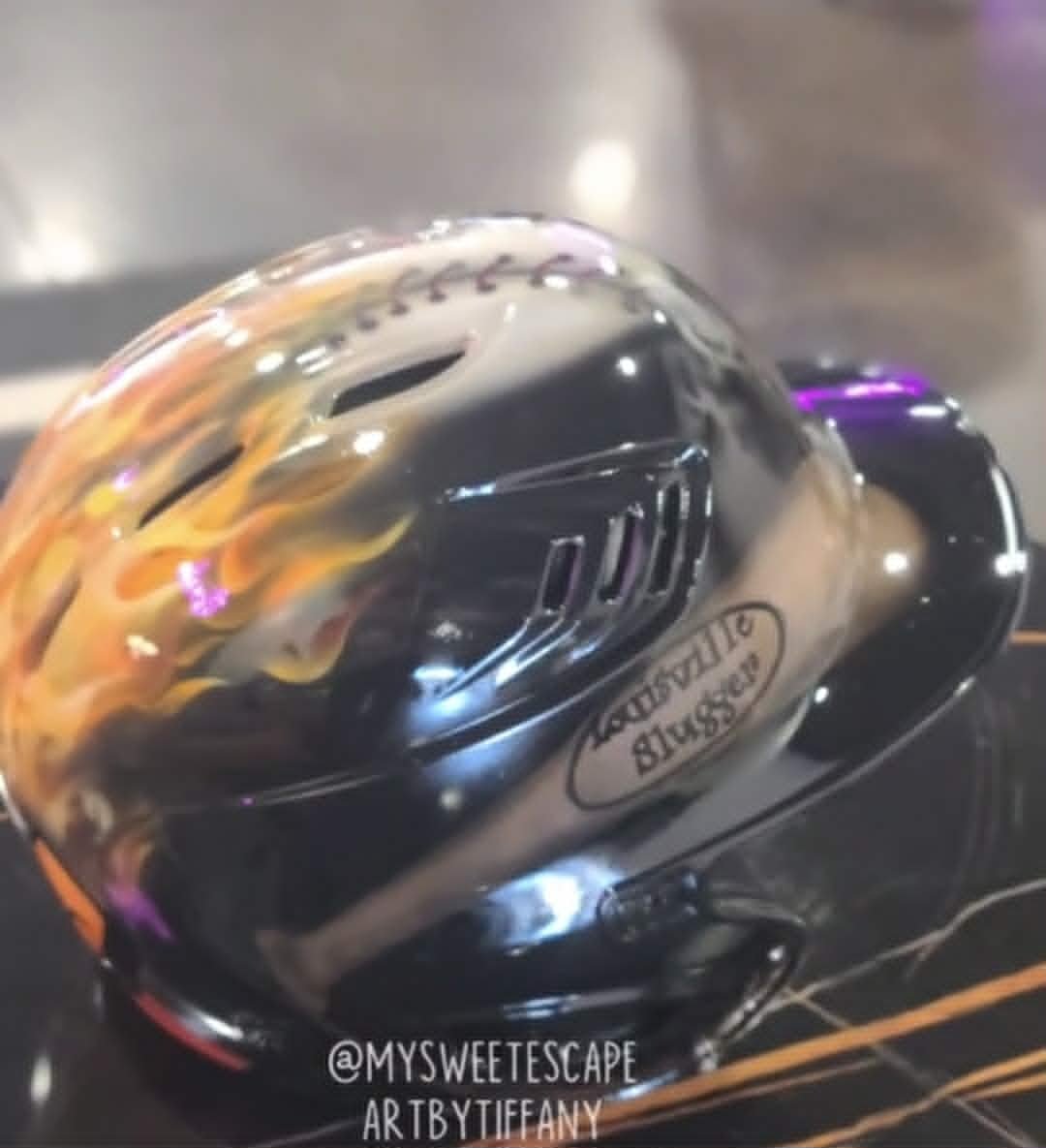 Custom airbrushed black Louisville Slugger batting helmet with realistic orange and yellow flames wrapping around the side