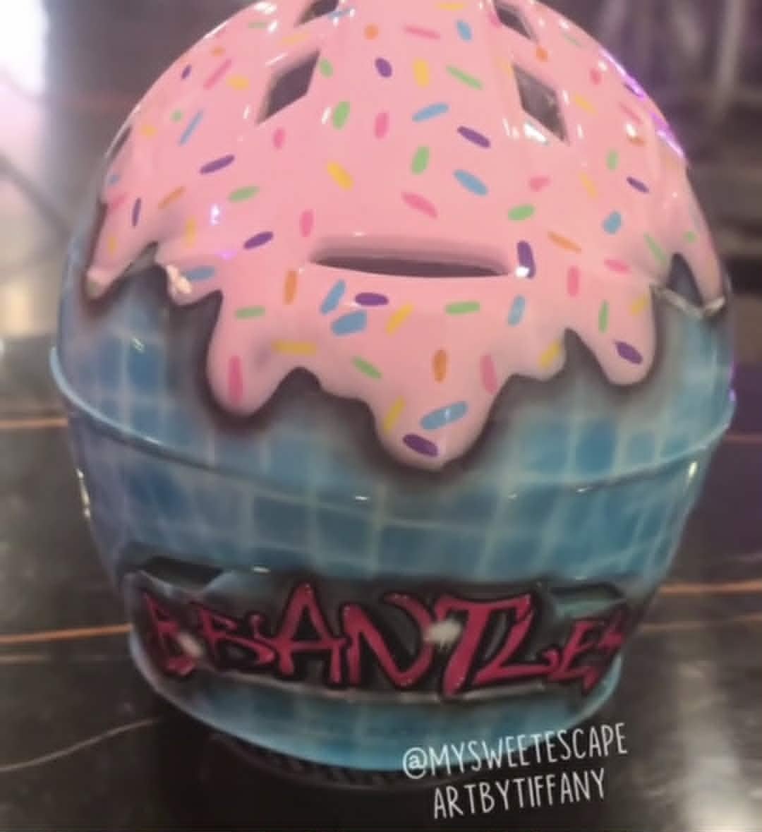 Custom airbrushed catcher's helmet for Brantley painted as an ice cream cone with pink frosting drips, rainbow sprinkles, and a blue waffle cone base