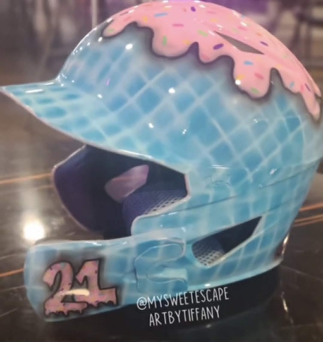 Custom airbrushed catcher's helmet painted as an ice cream cone with pink sprinkled frosting, blue waffle cone base, and number 21 on the ear flap