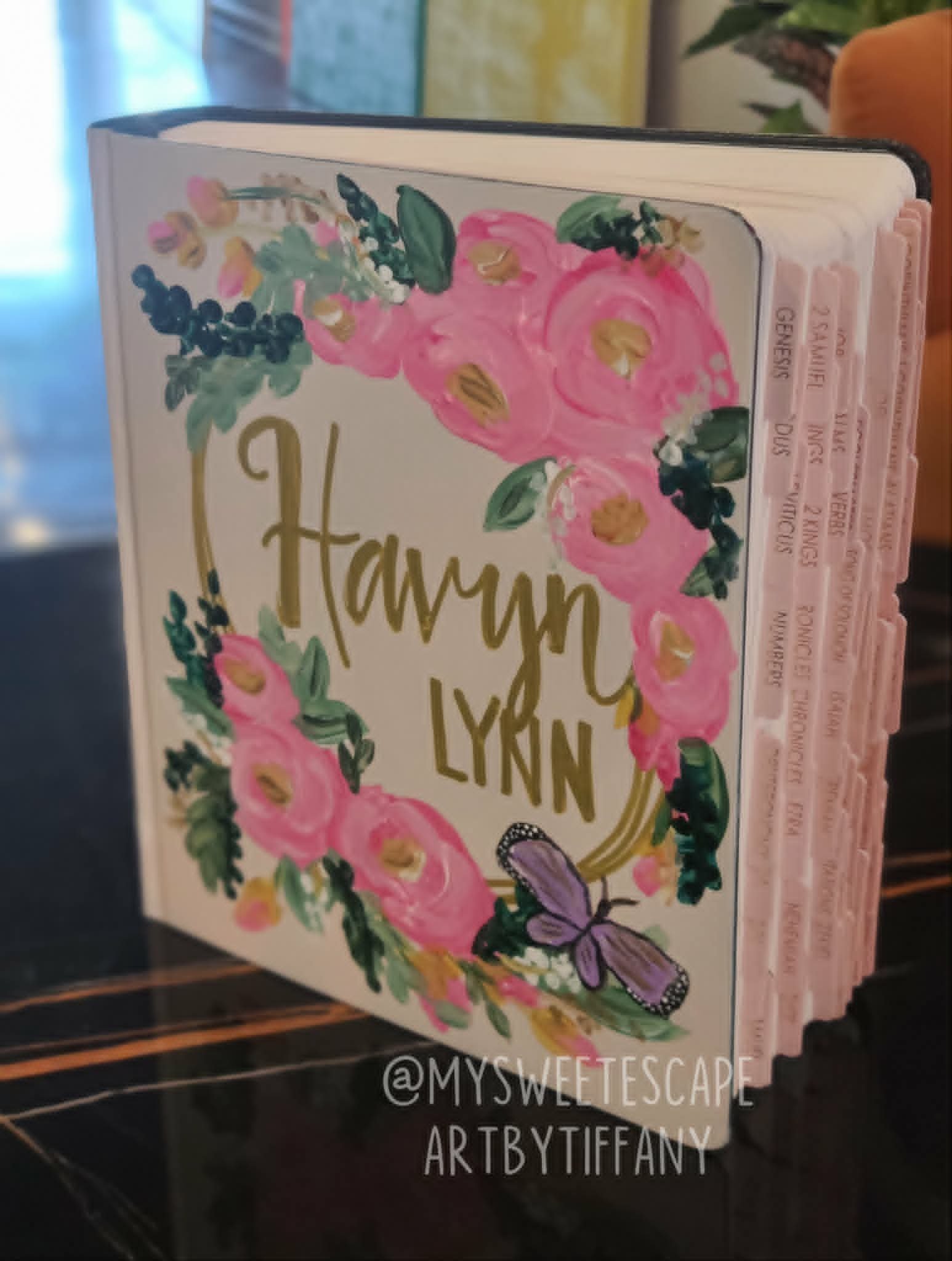 Hand-painted Bible cover for Hauryn Lynn with gold script lettering, pink rose wreath, and a purple butterfly accent