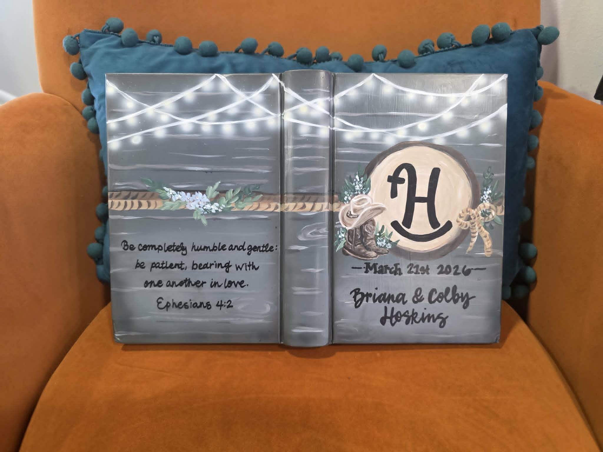 Hand-painted rustic wedding Bible for Briana and Colby Hoskins with barnwood background, string lights, cowboy boots, monogram H, and Ephesians 4:2
