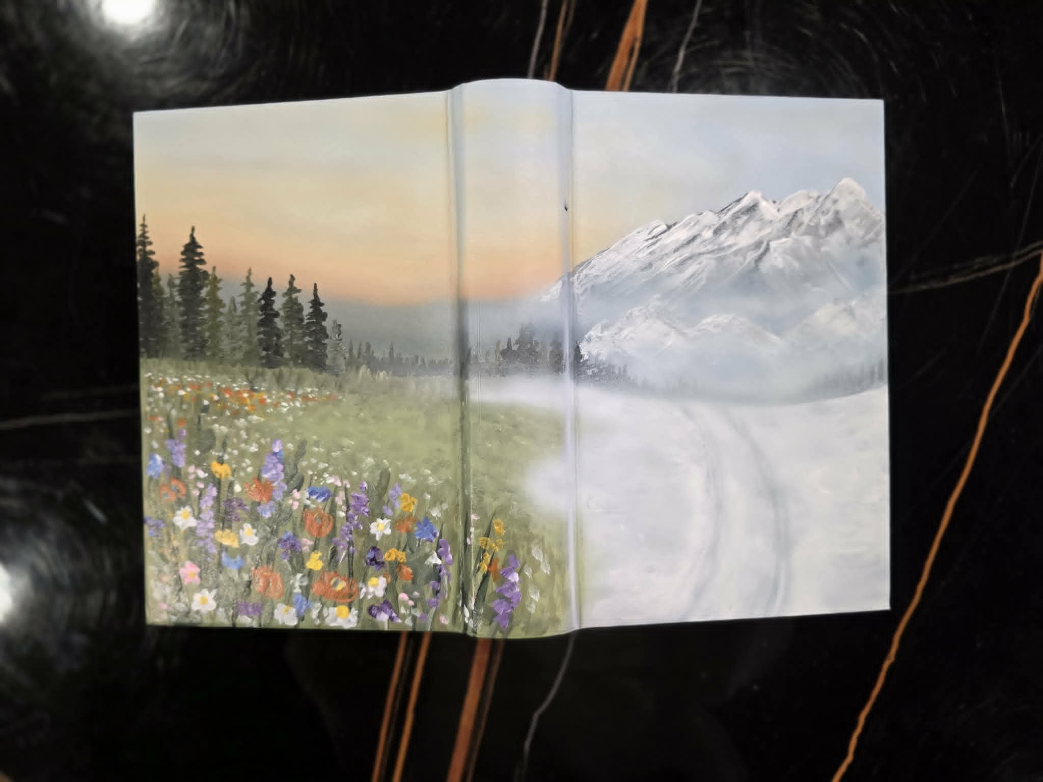 Hand-painted Bible cover with airbrushed mountain landscape, snowy peaks, evergreen trees, and a wildflower meadow at sunset