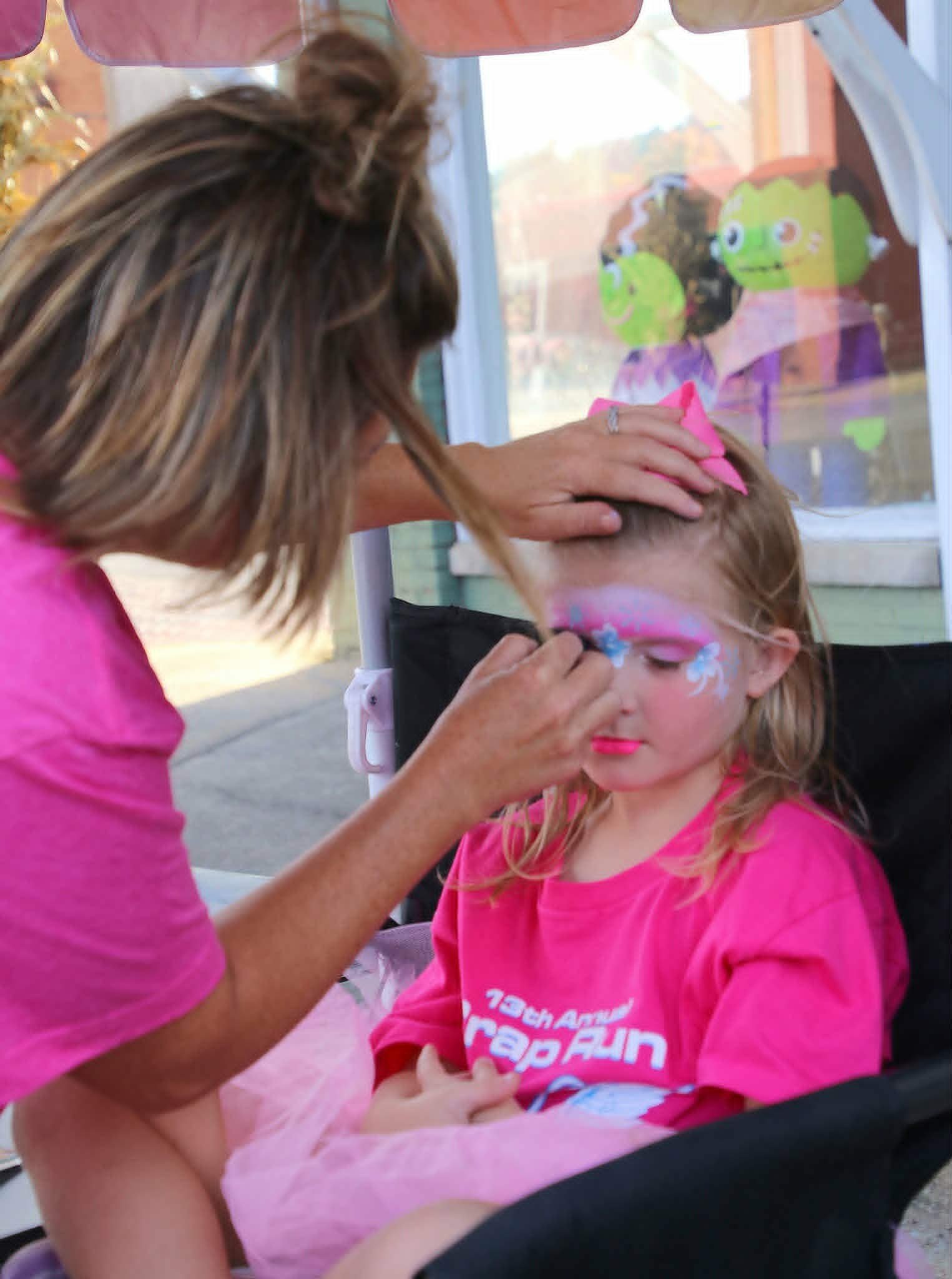 Two young girls smiling at a downtown event with pastel pink and unicorn-style face paint and matching pink hair bows