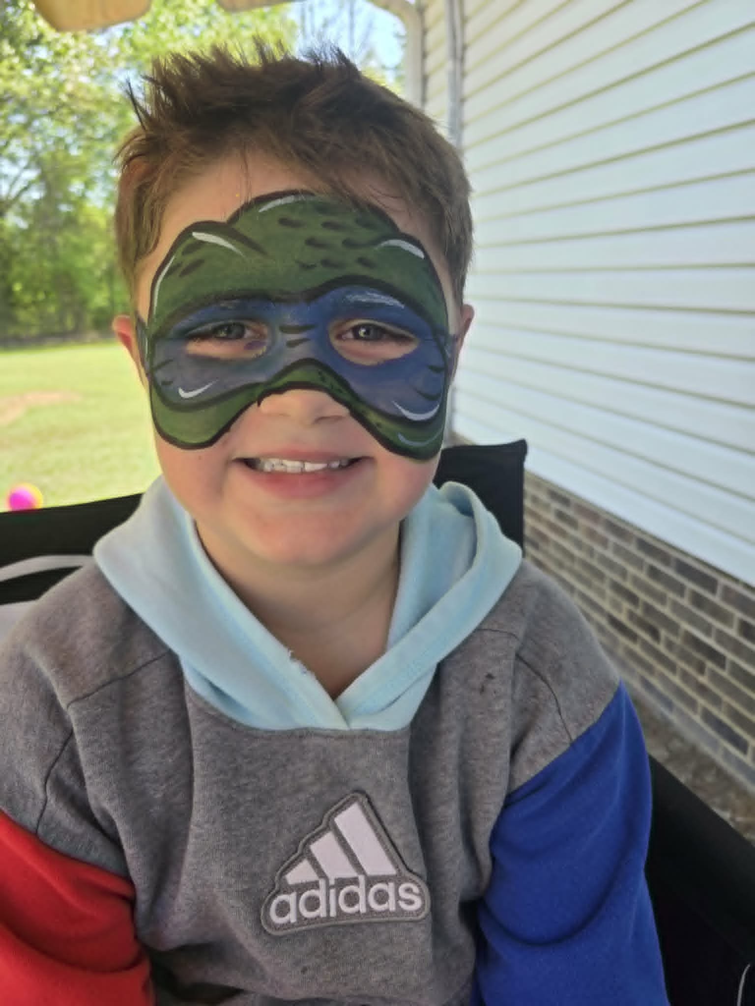 Green and blue Teenage Mutant Ninja Turtle mask face paint on a smiling young boy
