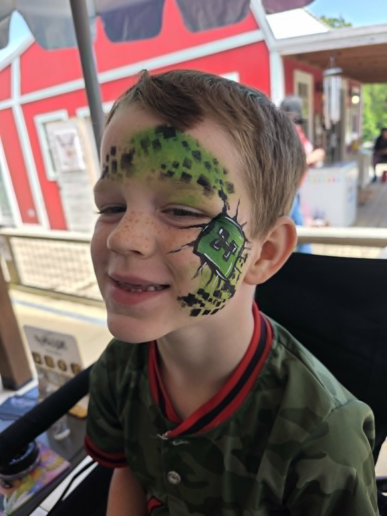 Minecraft Creeper-themed face paint with green pixel block design on a young boy in a baseball jersey