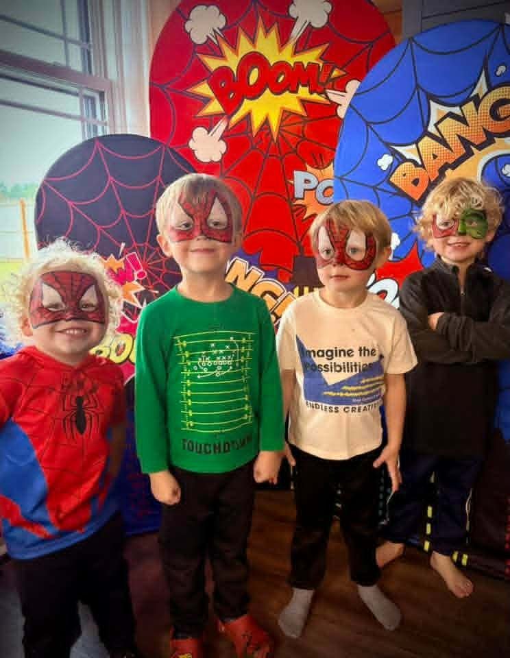 Group of four young boys with detailed Spider-Man and Green Lantern superhero mask face paint posing in front of a comic-book style backdrop