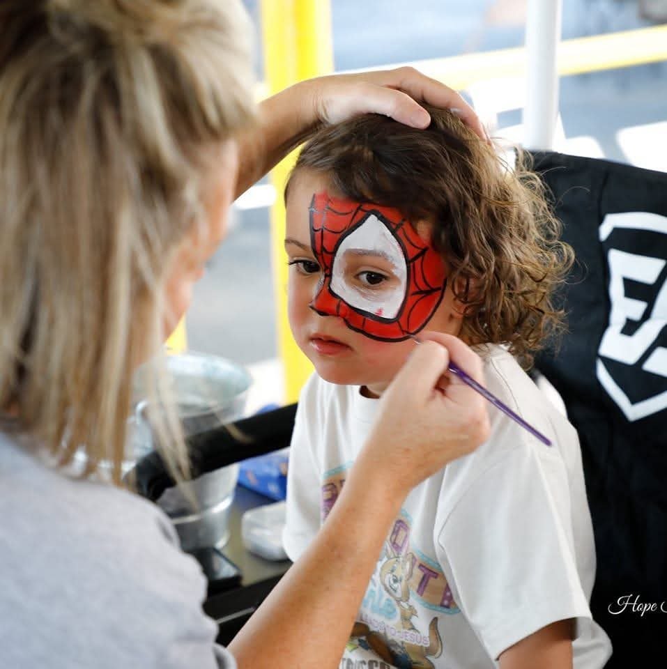 Tiffany painting a detailed Spider-Man mask with intricate webs on a young boy at an outdoor event