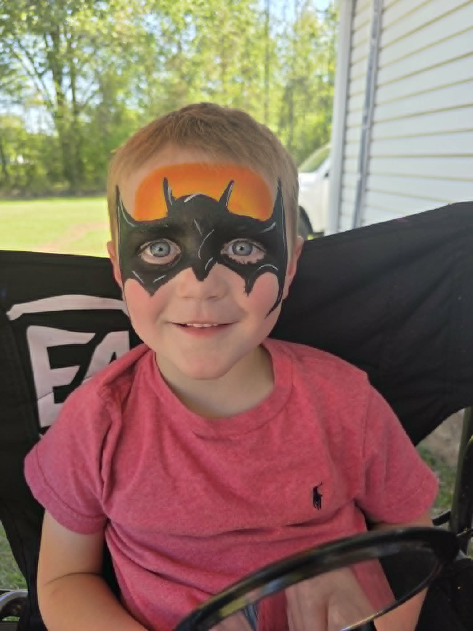 Bold black-and-orange Batman mask face paint with sunset accent on a young boy