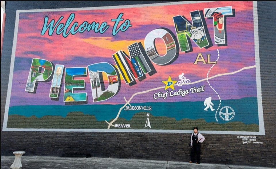 Welcome to Piedmont, AL postcard-style mural with map of Chief Ladiga Trail and Tiffany standing in front