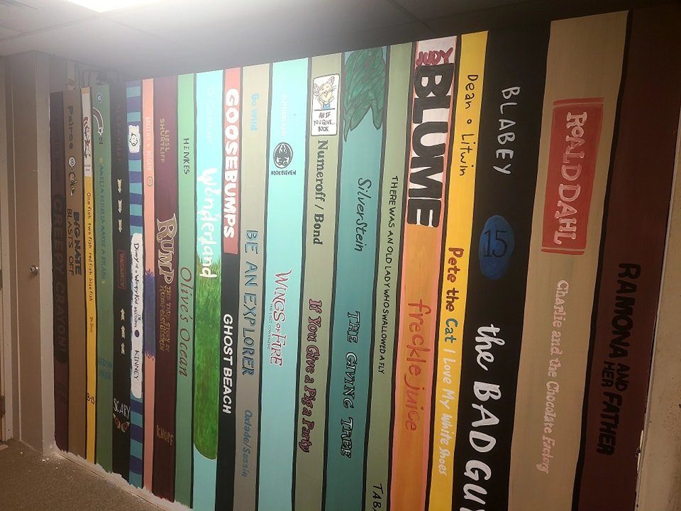 Library mural painted as a row of giant book spines featuring Roald Dahl, Judy Blume, Goosebumps, and other classic titles