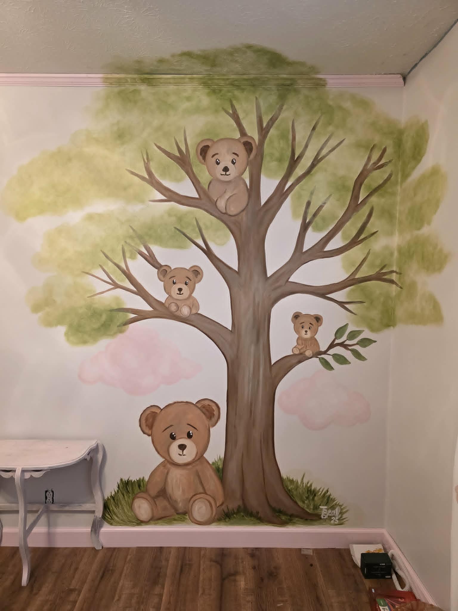 Nursery mural of a soft green tree with four cuddly teddy bears nestled in the branches and at the base, set against pink clouds
