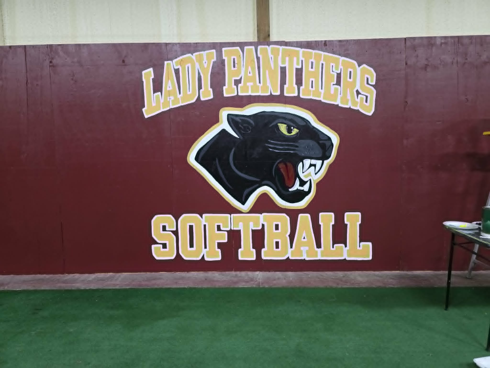 Lady Panthers Softball indoor batting cage mural with a fierce black panther head logo, gold and white outlined team lettering on a maroon wall