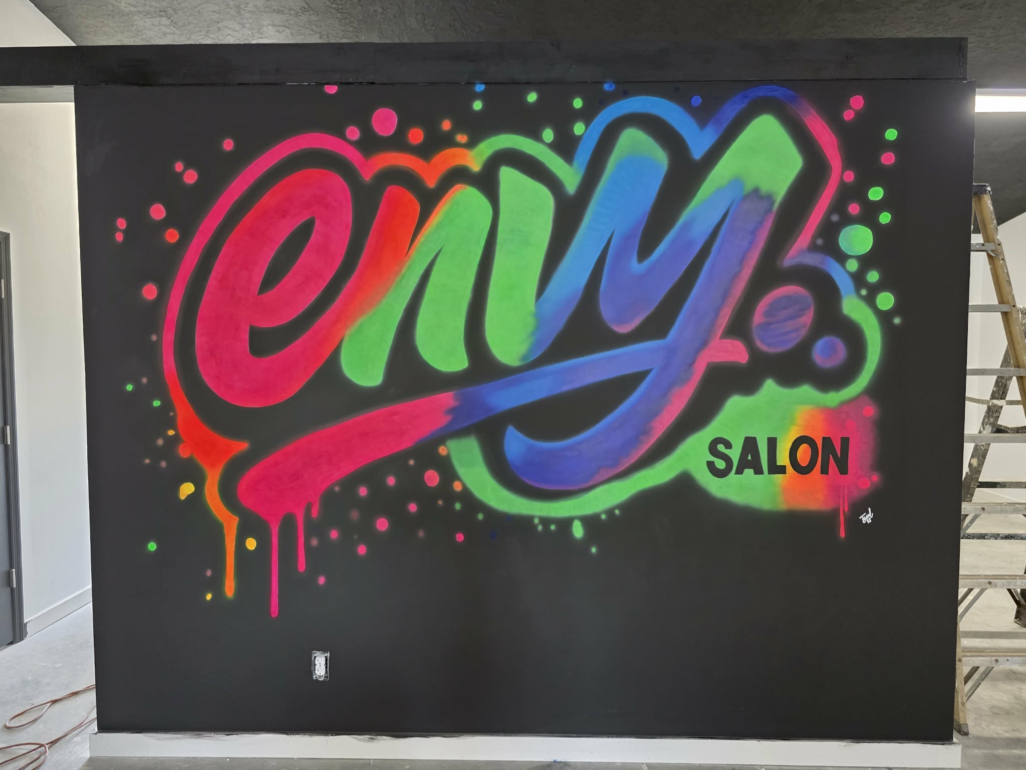 Envy Salon graffiti-style mural with vibrant pink, green, blue, and purple bubble lettering and dripping paint accents on a black wall
