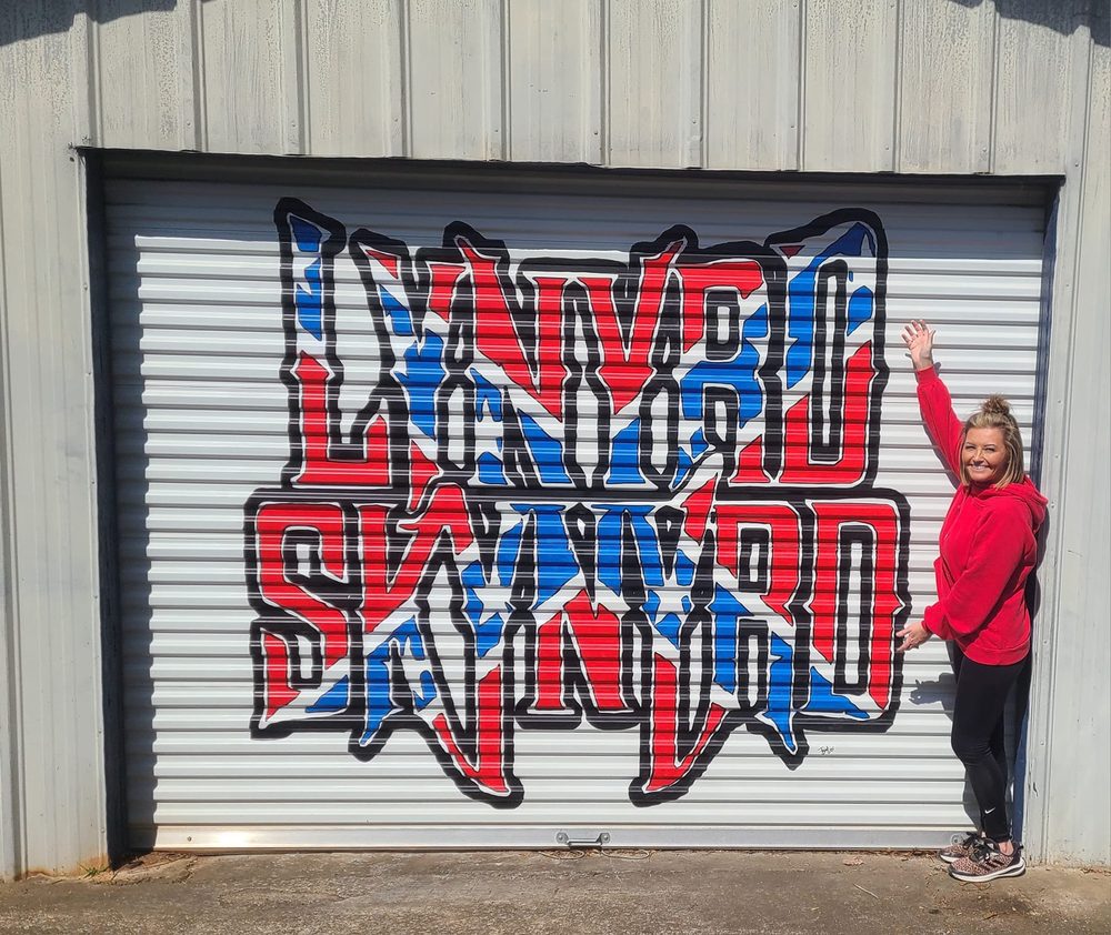 Lynyrd Skynyrd graffiti-style mural on a metal garage door with Tiffany standing beside it