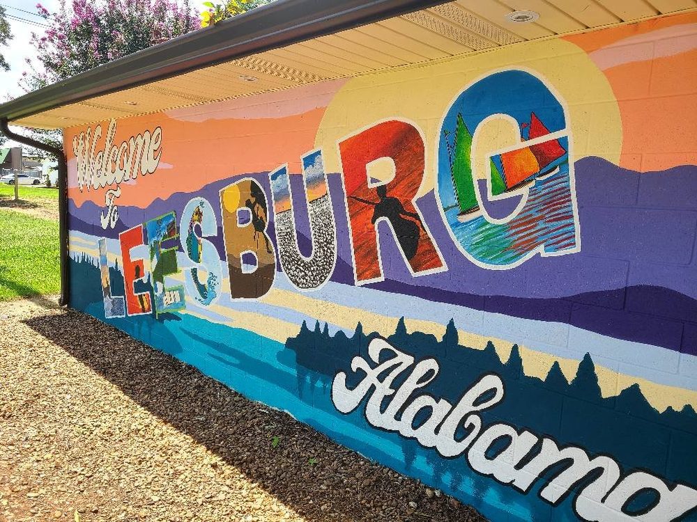 Welcome to Leesburg, Alabama postcard-style mural with sailboats, sunset, and lake scenery inside the letters