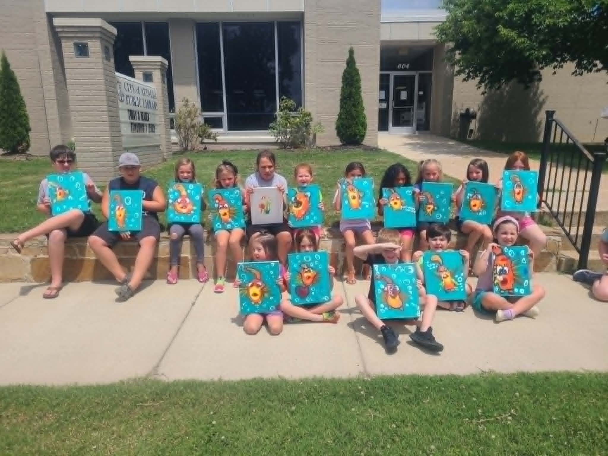 Group of kids in front of the Attalla Public Library holding up their finished SpongeBob-style underwater paintings