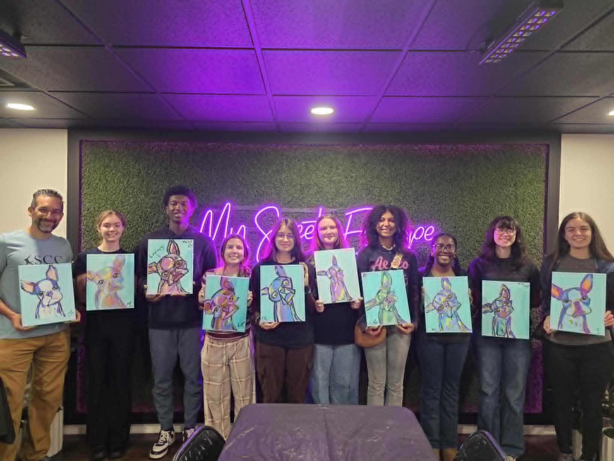 SCC student group paint party in the My Sweet Escape studio holding up their finished colorful abstract chihuahua paintings on teal backgrounds