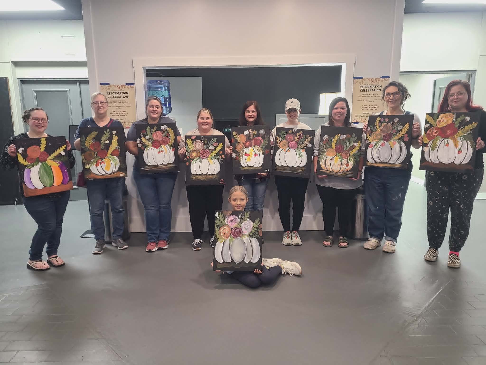 Reformation Celebration paint party group at Redeemer Church holding up their finished white pumpkin paintings topped with autumn floral arrangements