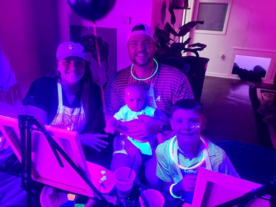 Family with two young kids and a baby posing with glow necklaces at a blacklight paint party