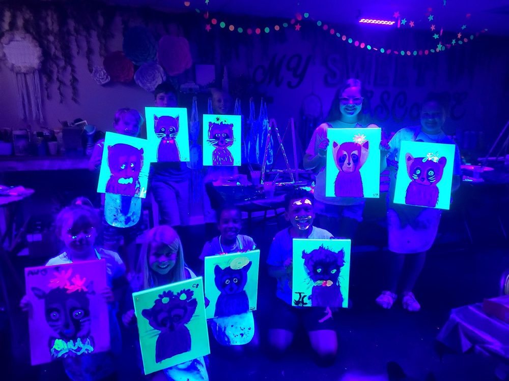 Group of kids holding up their glowing cat paintings at a blacklight paint party