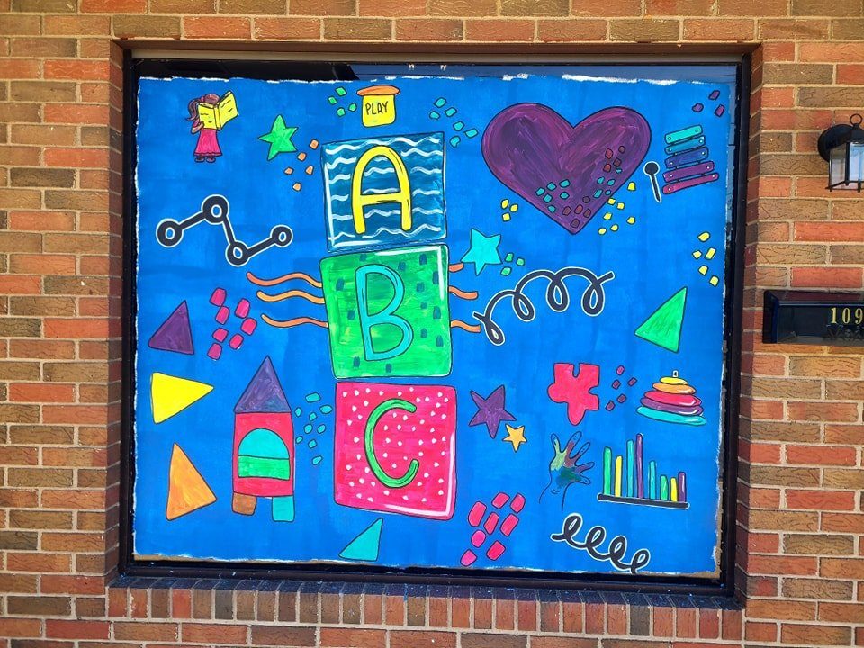 Colorful daycare window painting featuring stacked ABC blocks, toys, and playful shapes