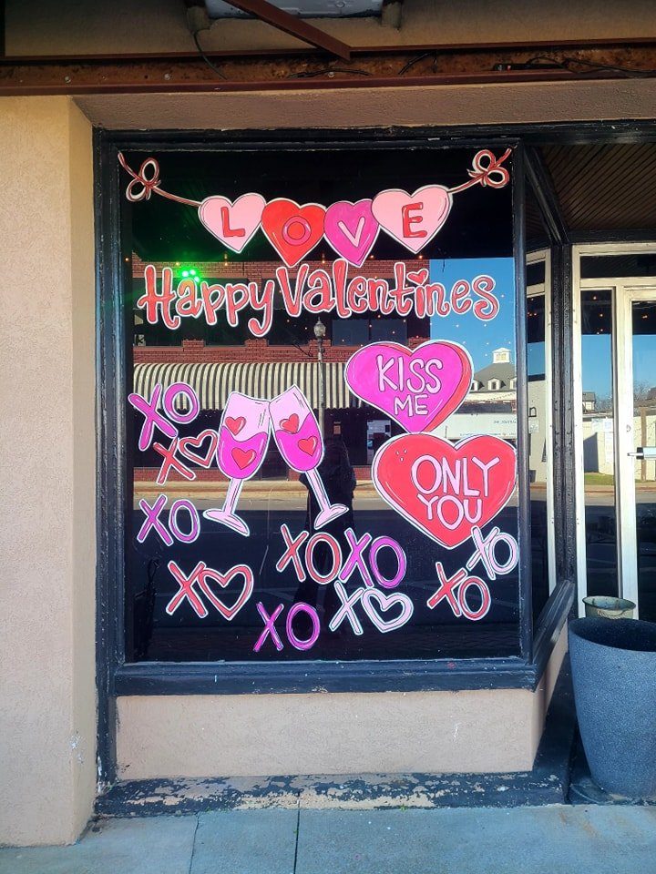 Happy Valentine's Day window painting with hearts, champagne glasses, and 'Kiss Me' candy hearts
