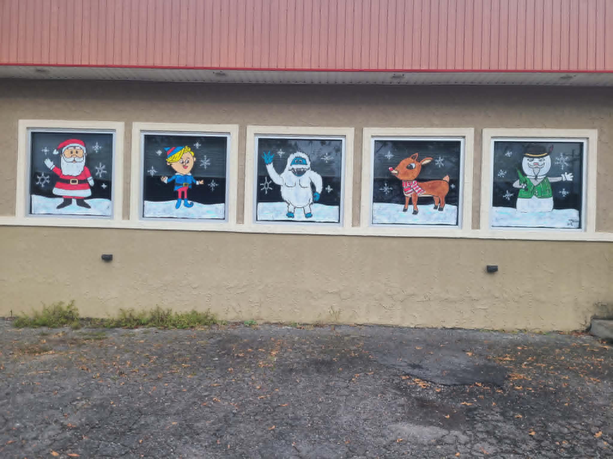 Christmas storefront windows painted with the cast of Rudolph the Red-Nosed Reindeer — Santa, Hermey the elf, the Bumble, Rudolph, and Sam the Snowman