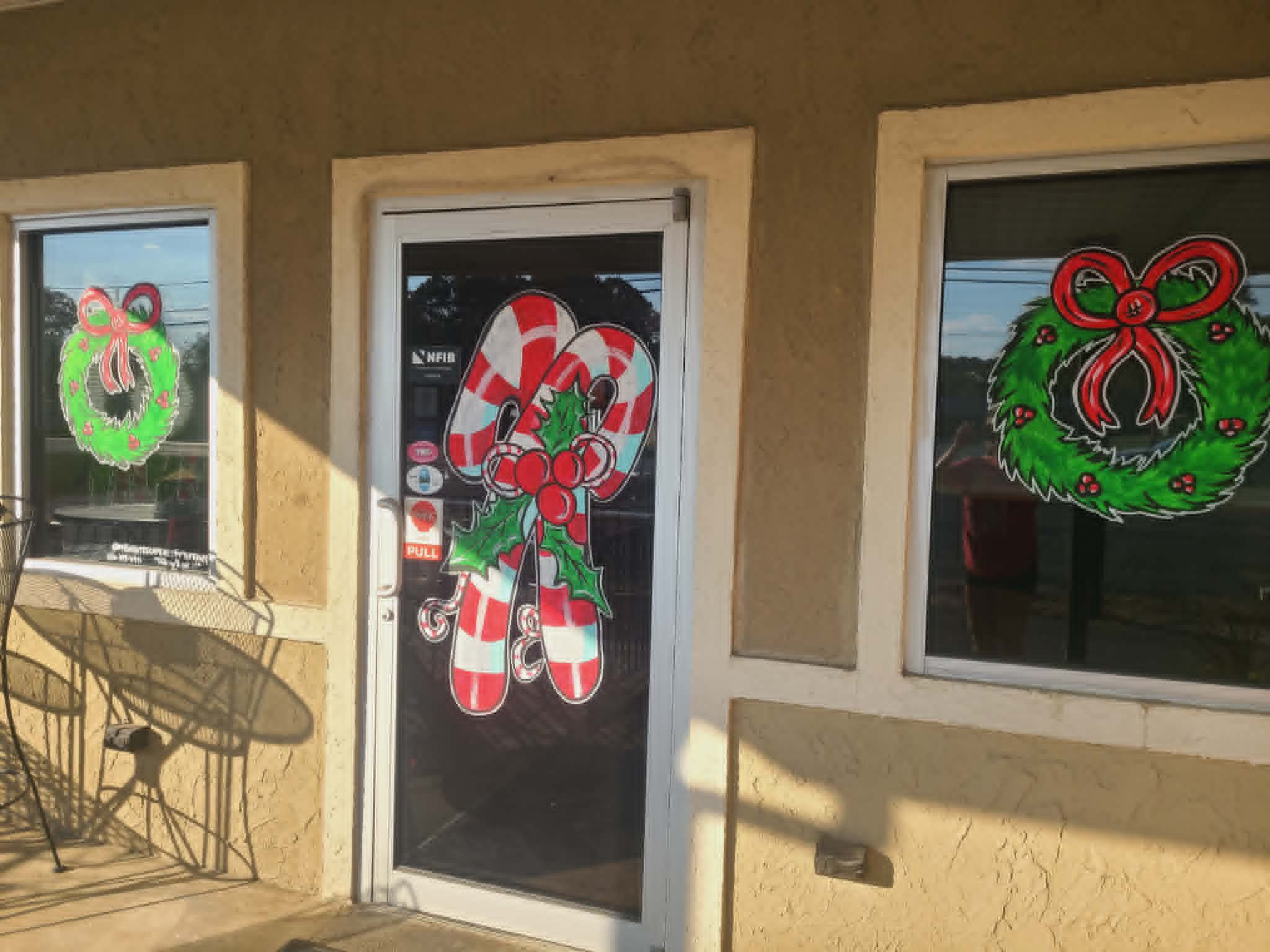 Christmas storefront painted with bow-topped wreaths on the windows and a holly-and-ribbon candy cane bouquet on the front door