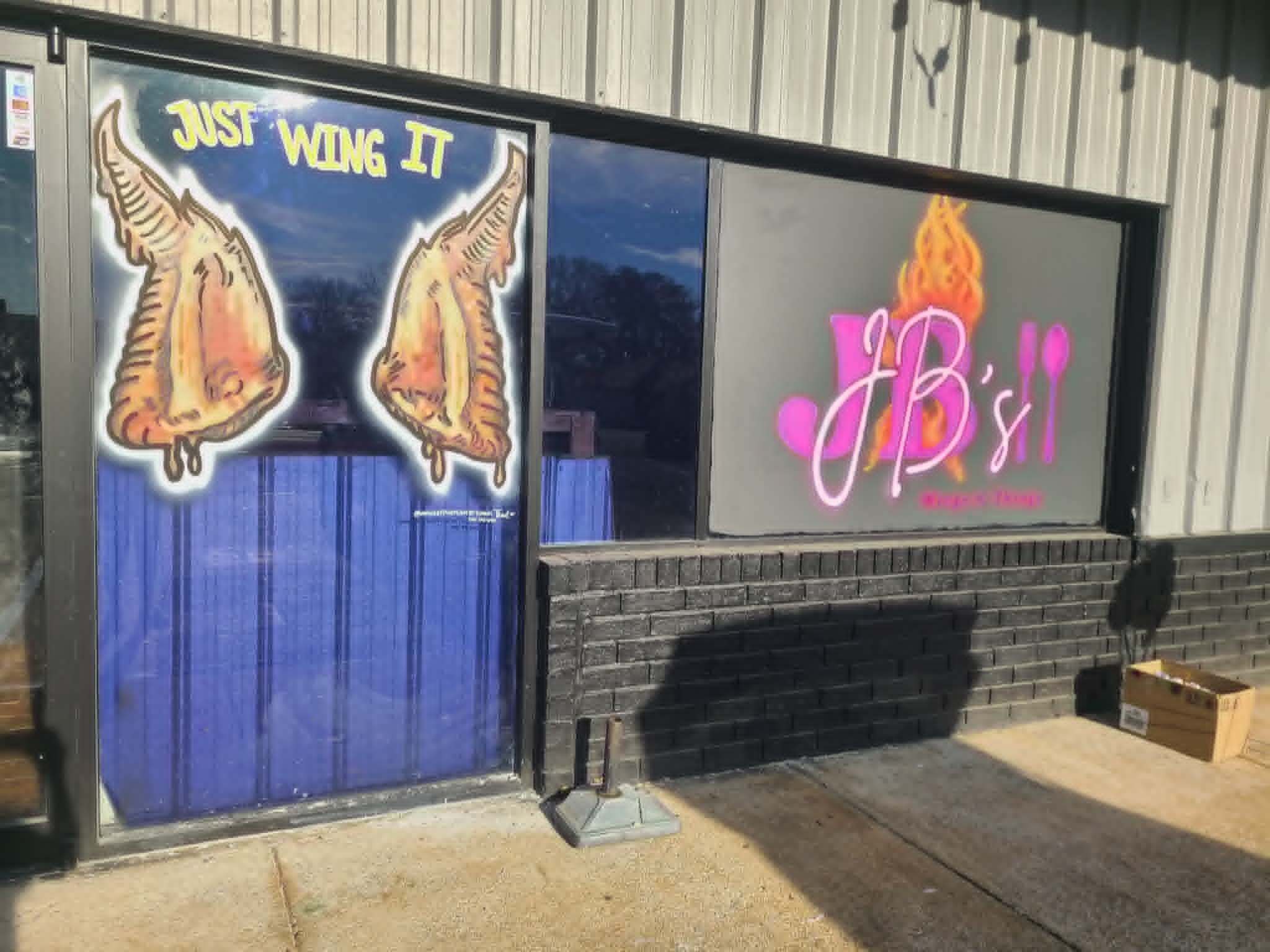 JB's Wings N Things storefront windows showing a 'Just Wing It' panel with two saucy chicken wings beside the main JB's logo window
